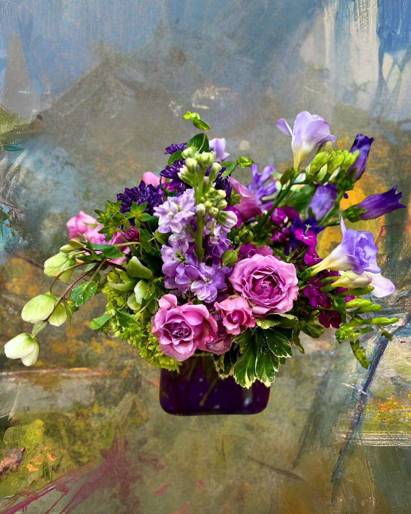 Purple and pink flower bouquet in a dark vase against a soft painted background