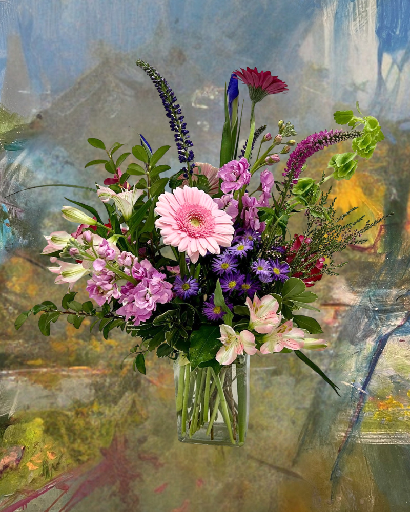 Mixed bouquet of pink, purple, and white flowers in a glass vase against an abstract painted background