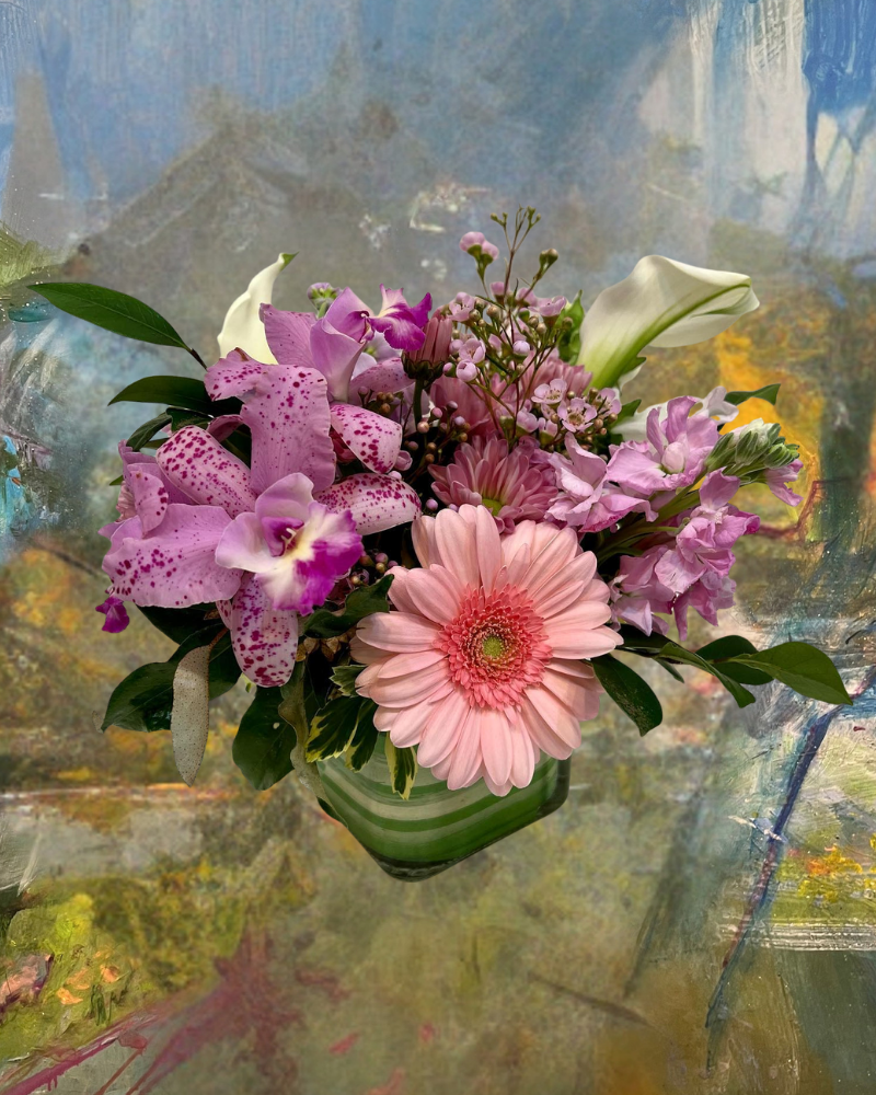 Pink and purple mixed flower bouquet in a green vase against an abstract painted background