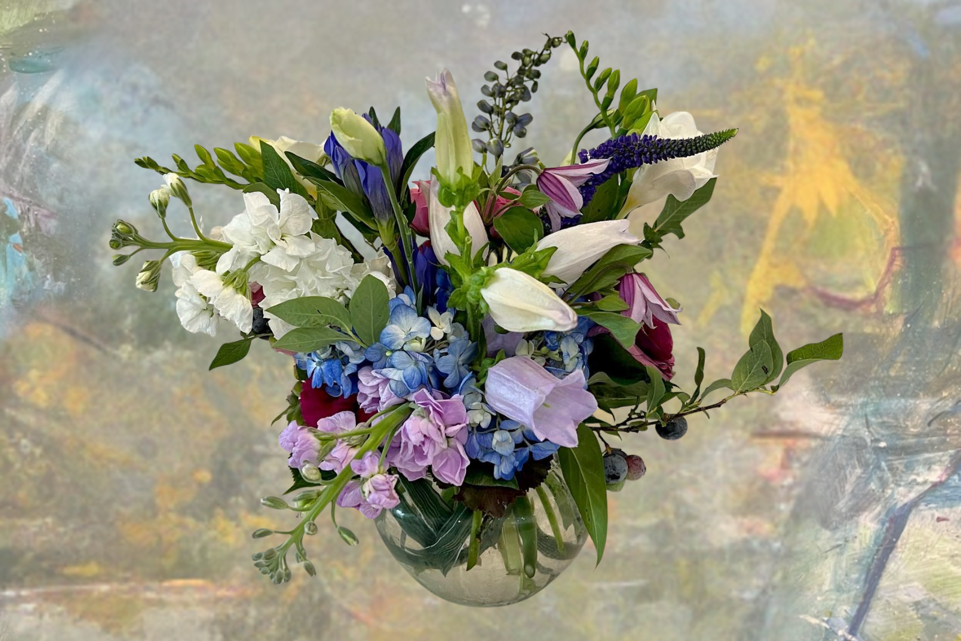 A colorful bouquet of white, blue, purple, and green flowers in a clear glass vase