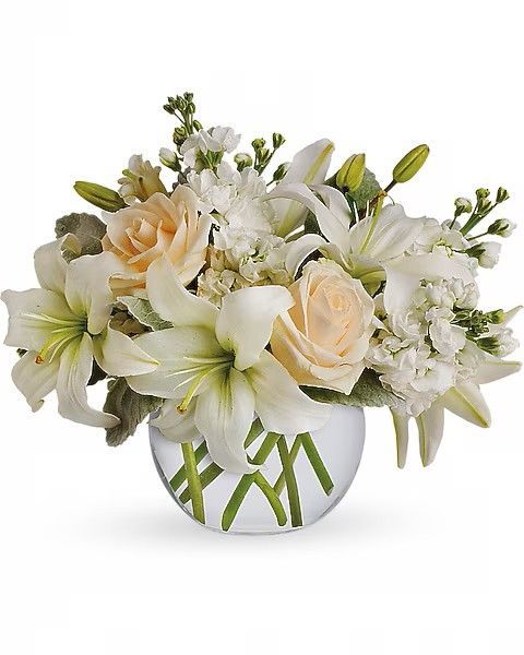 White and peach-colored flower arrangement in a clear glass bowl, includes lilies and roses.