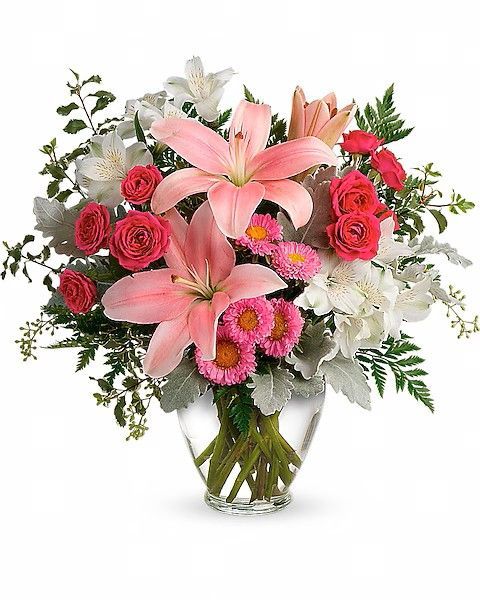 Bouquet of pink lilies, roses, and daisies in a clear vase with greenery.