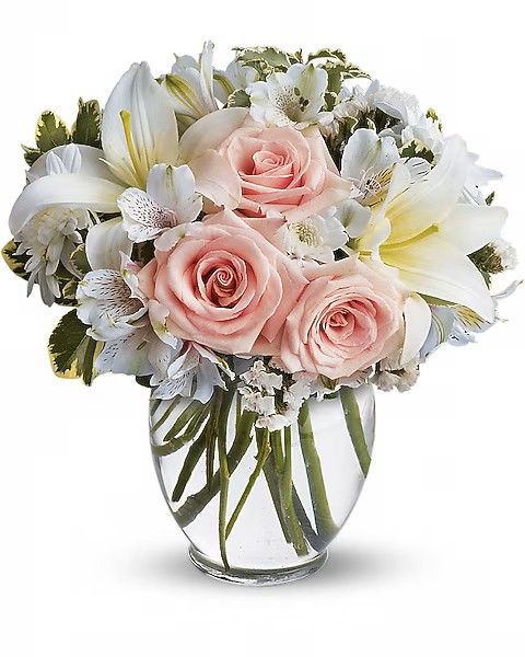 Bouquet of pink roses, white lilies, and other white flowers in a clear glass vase.