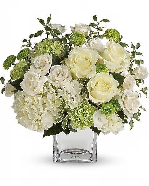 White roses, hydrangeas, and green accents in a square glass vase.
