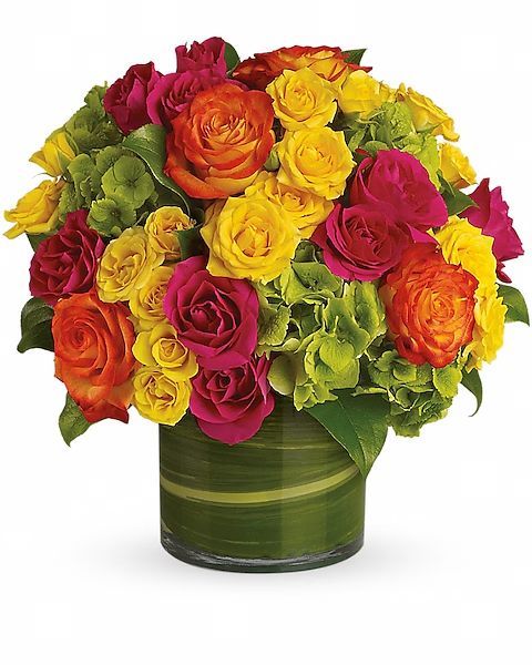 Vibrant floral arrangement in a cylindrical glass vase. Features roses in yellow, orange, and magenta, with green foliage.