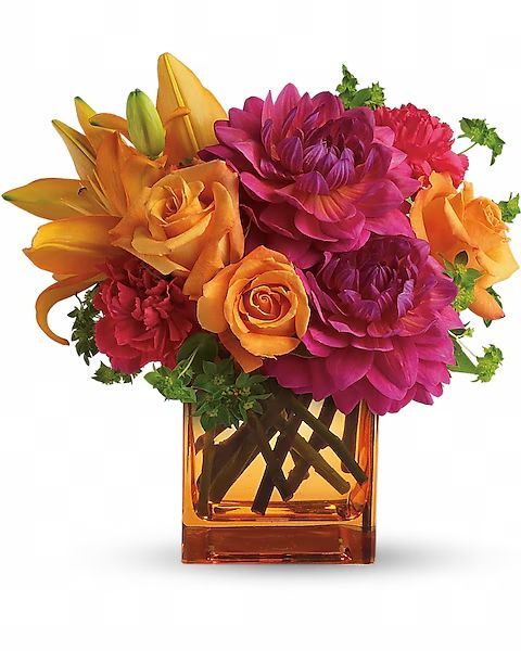 Bouquet of orange roses, lilies, pink dahlias, and red carnations in an orange square vase.
