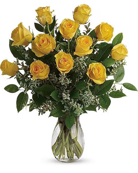 Yellow roses in a clear glass vase, surrounded by green foliage.