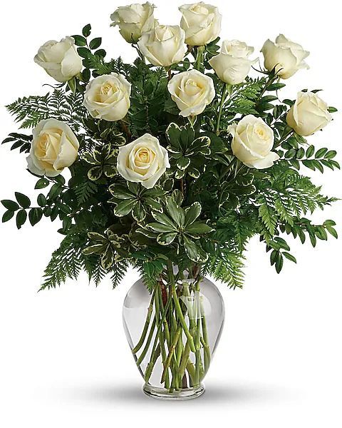 Bouquet of white roses in a clear glass vase, surrounded by green foliage.