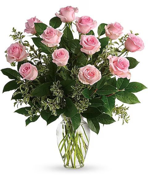 Pink roses in a clear glass vase with green foliage.
