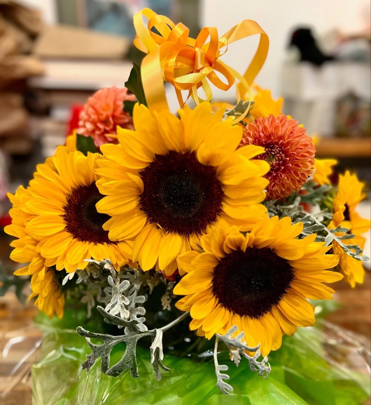 Sunflowers and orange mums in a bouquet, tied with an orange ribbon.