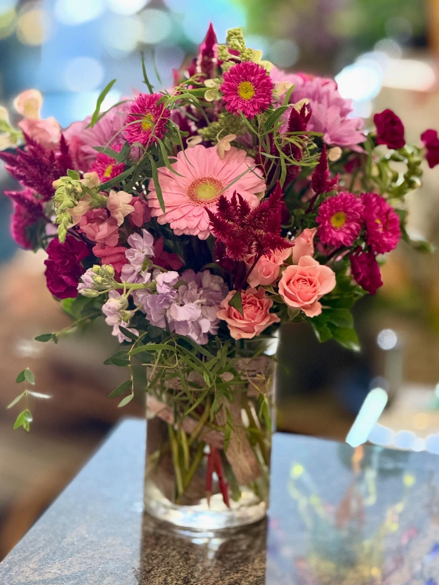 Vibrant bouquet of pink, purple, and red flowers in a clear vase wrapped with twine, set on a dark surface.