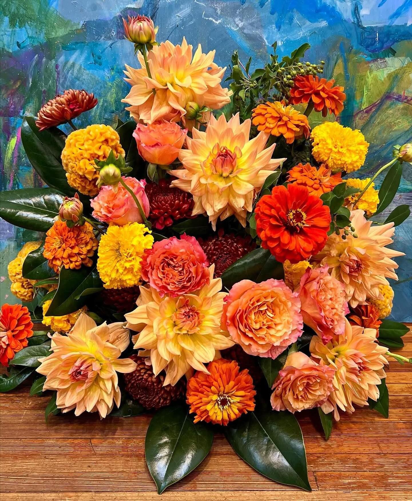 Colorful floral arrangement with orange and yellow dahlias, zinnias, and roses.