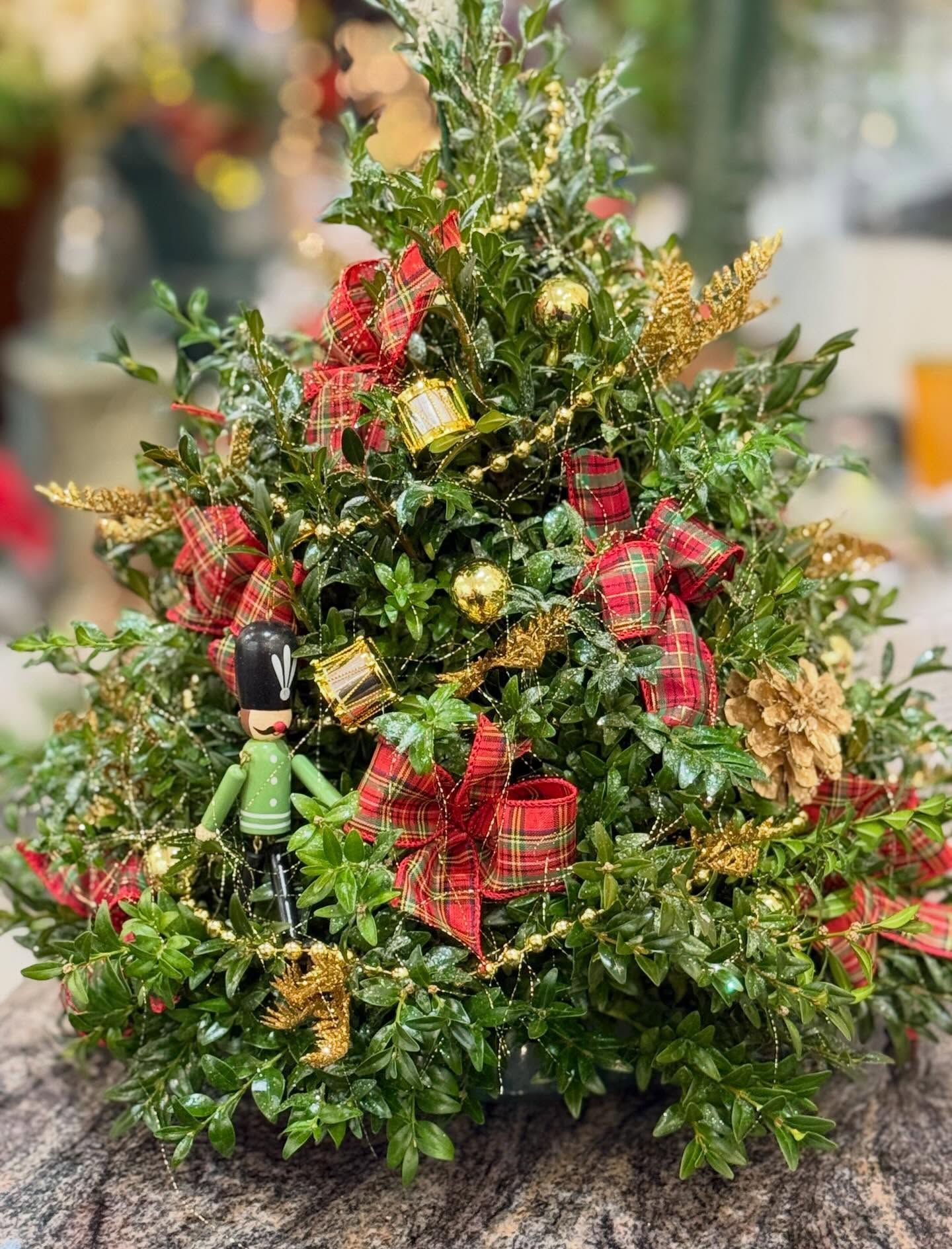 Christmas tree arrangement with green foliage, red plaid bows, gold ornaments and a toy soldier.
