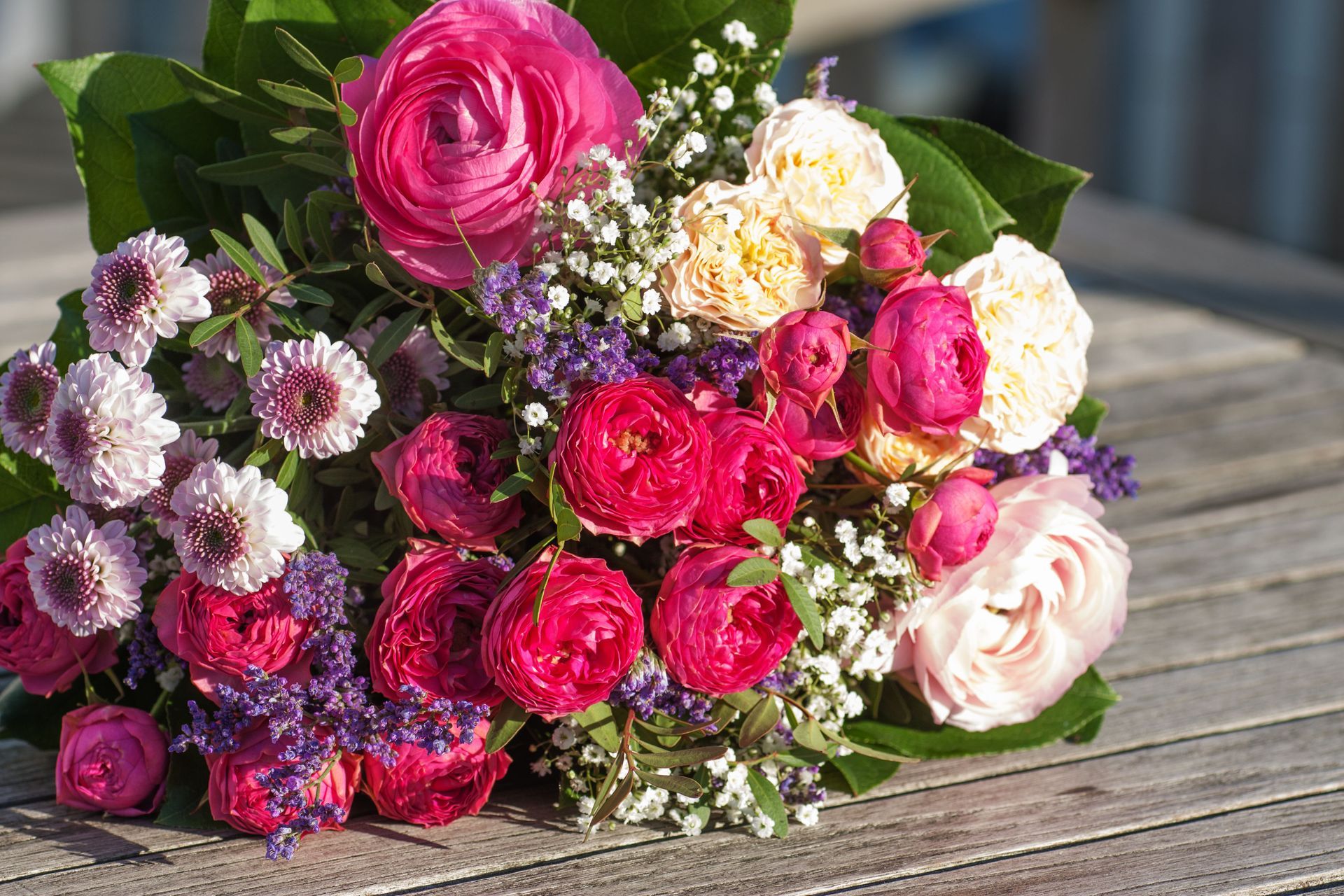 Bouquet of pink, red, and peach flowers with green foliage on a wooden table.