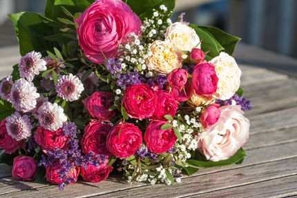 Bouquet of pink, red, and peach flowers with green foliage on a wooden table.