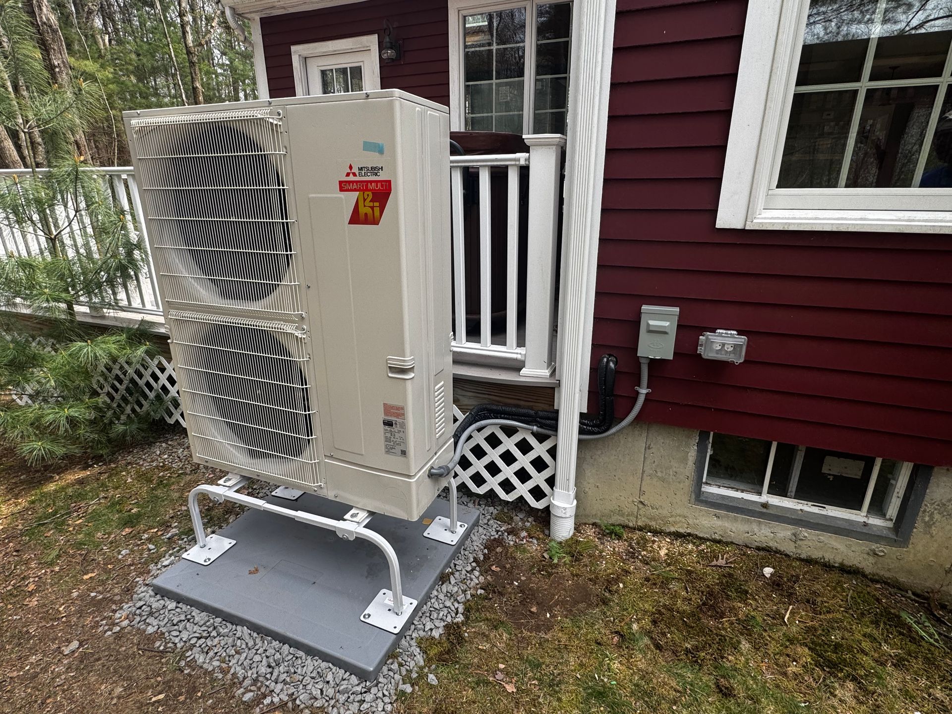 A large air conditioner is sitting on the side of a red house.