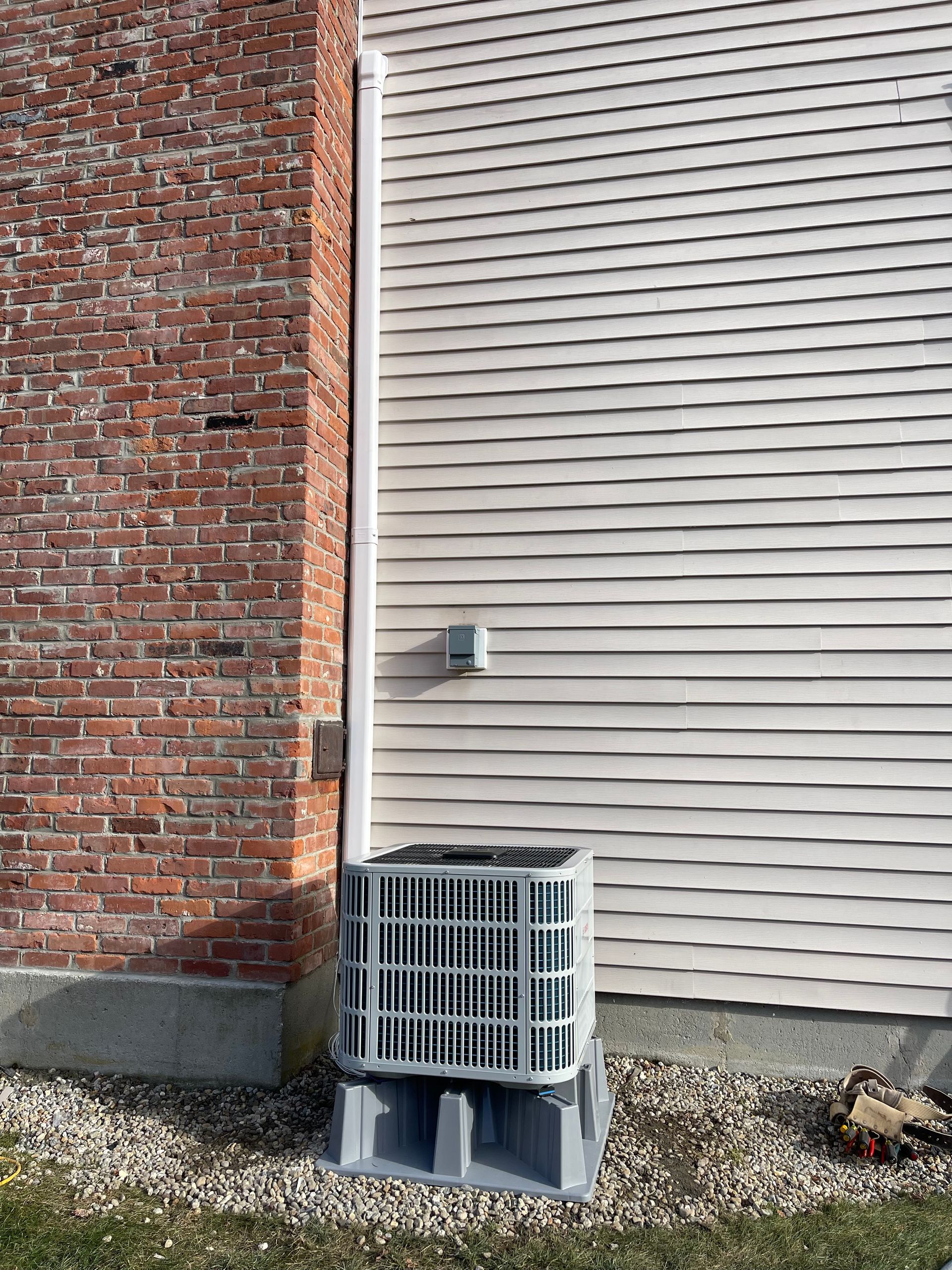 An air conditioner is installed on the side of a brick house.
