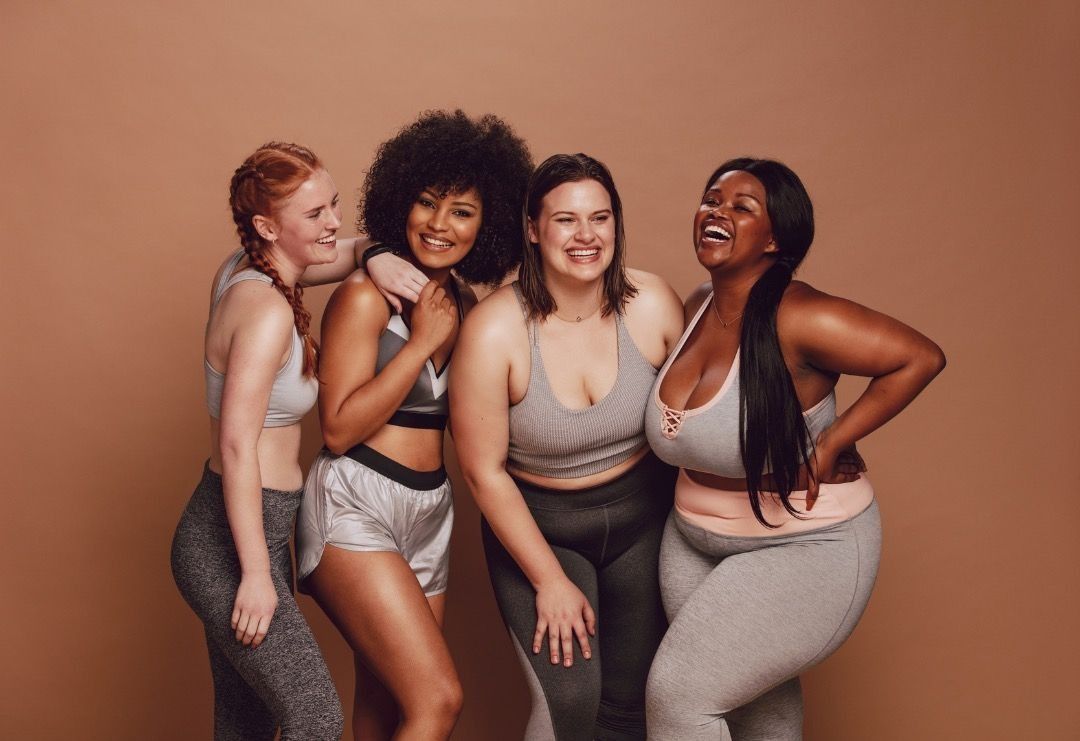 Four women posing together in workout clothes against a plain brown background.