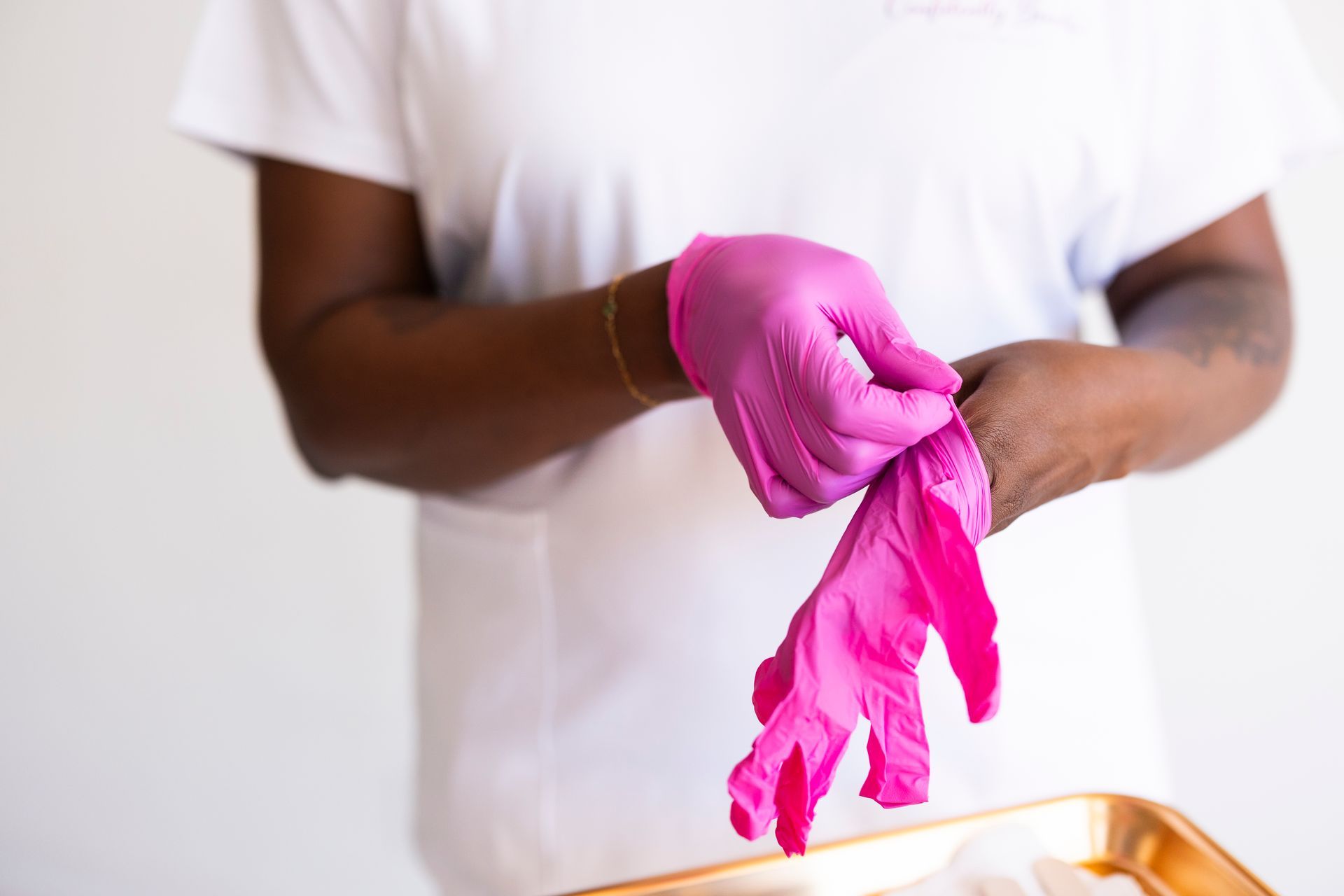 Person putting on bright pink gloves over a metal tray in a white shirt