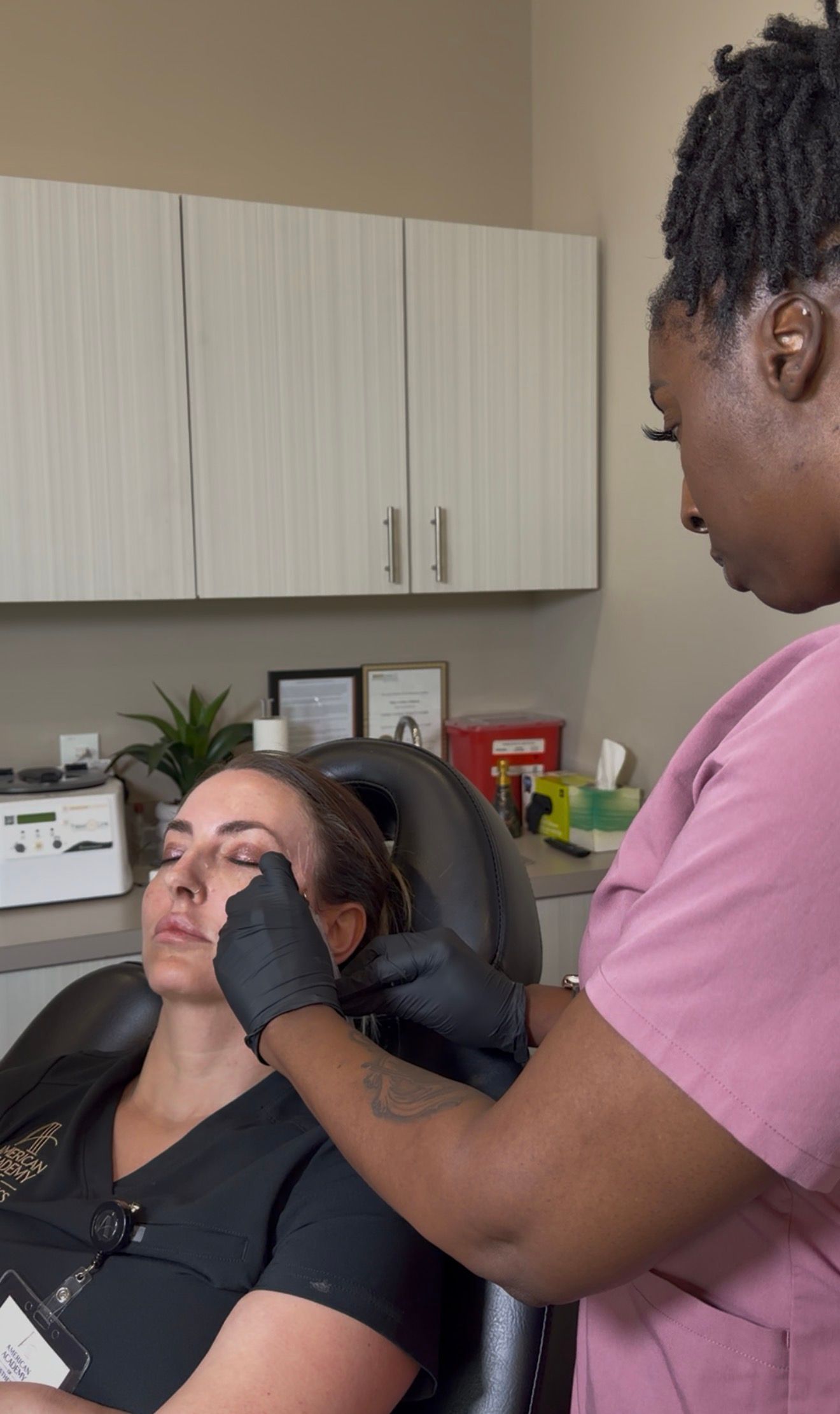 A woman applies makeup to another woman seated in a salon chair.