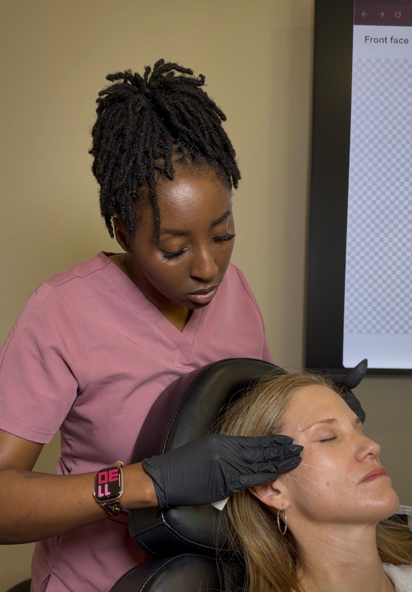 A clinician wearing gloves treats a seated patient's face in a medical office.