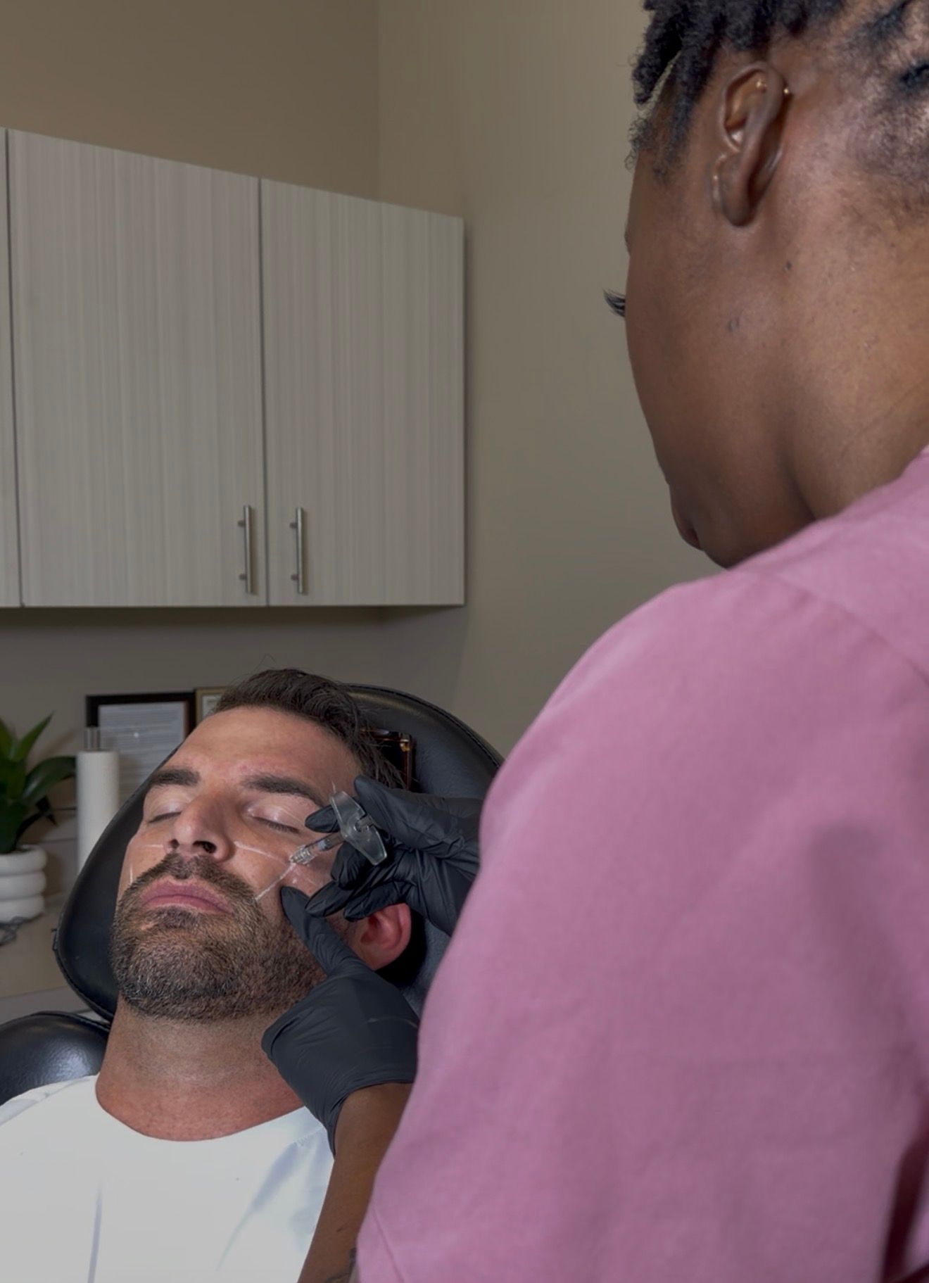 A person receiving an eyebrow treatment while another technician works nearby in a salon setting