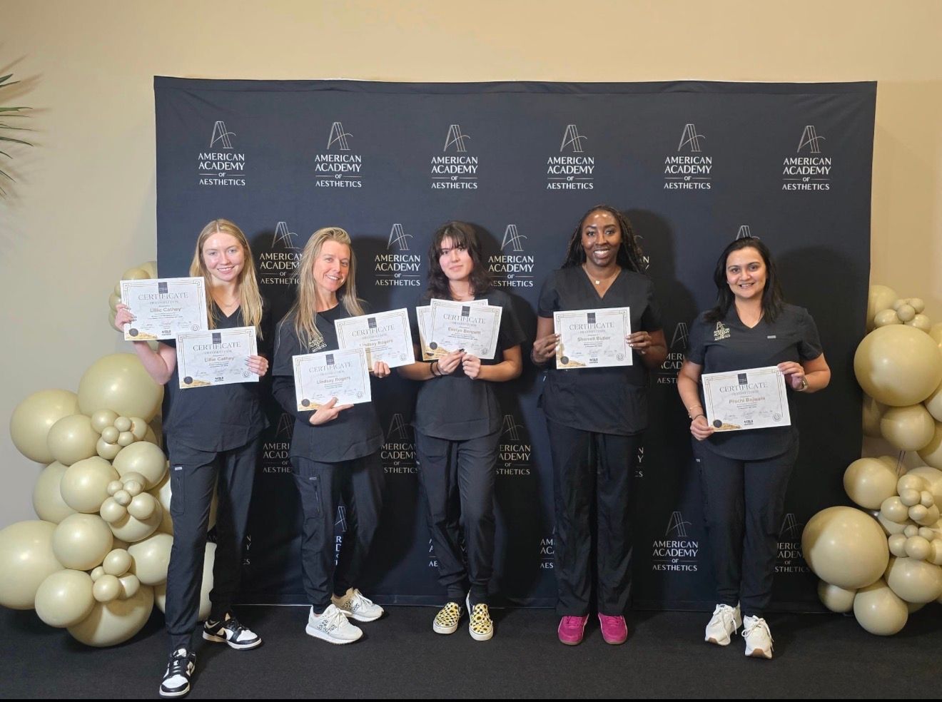 Five people in dark outfits hold certificates at a black-and-gold awards ceremony backdrop