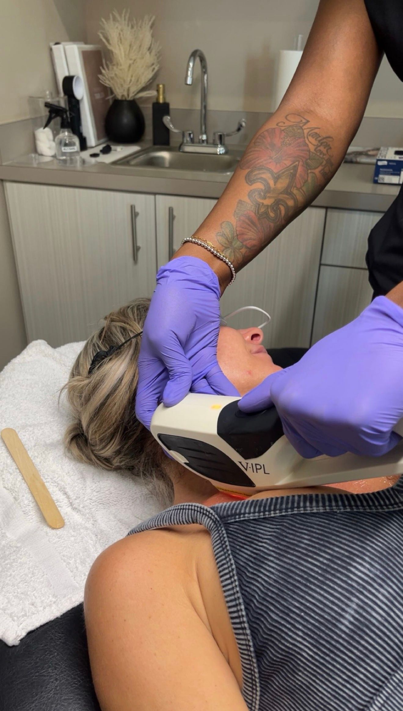 Gloved technician using a handheld device on a client’s neck in a salon treatment room