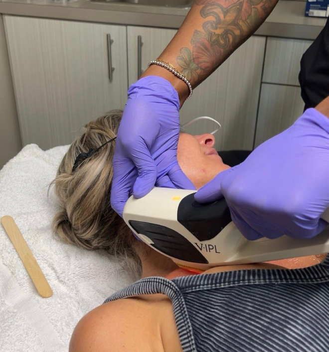 Gloved clinician applying a face treatment to a reclining patient in a clinic room