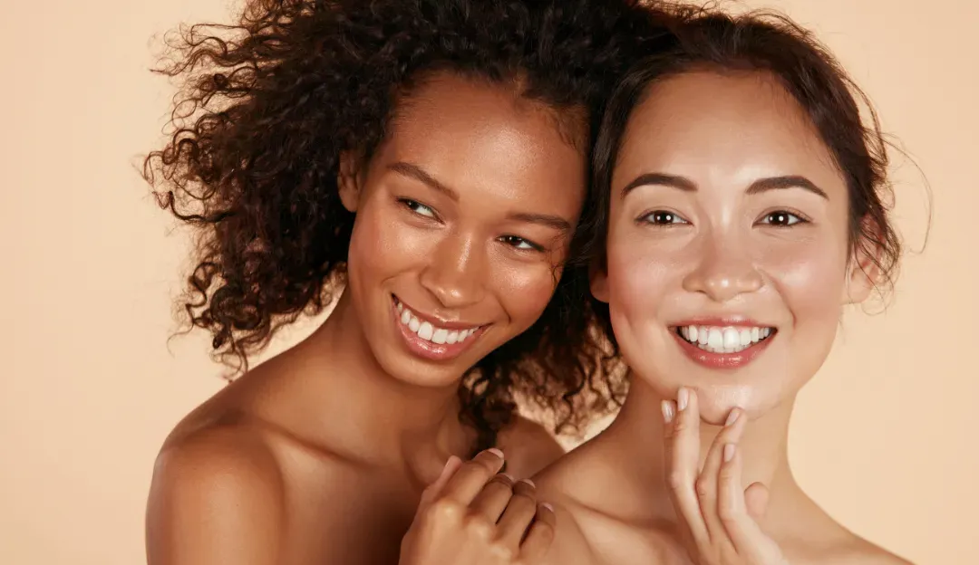 Two smiling women posing close together against a warm beige background.