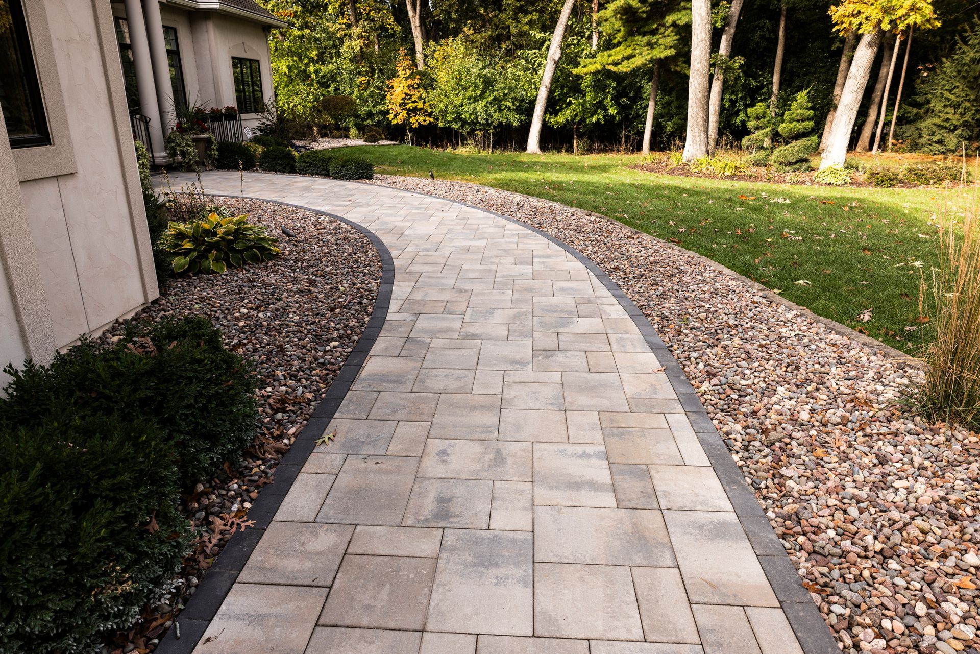 A brick walkway leading to a house with trees in the background.