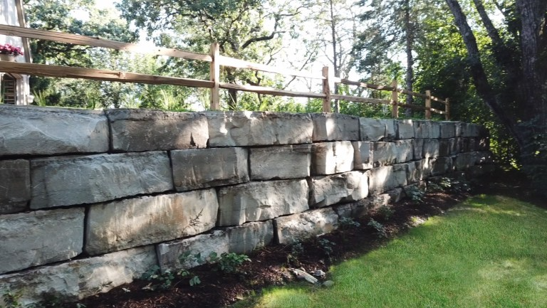 A stone wall with a wooden fence in the background