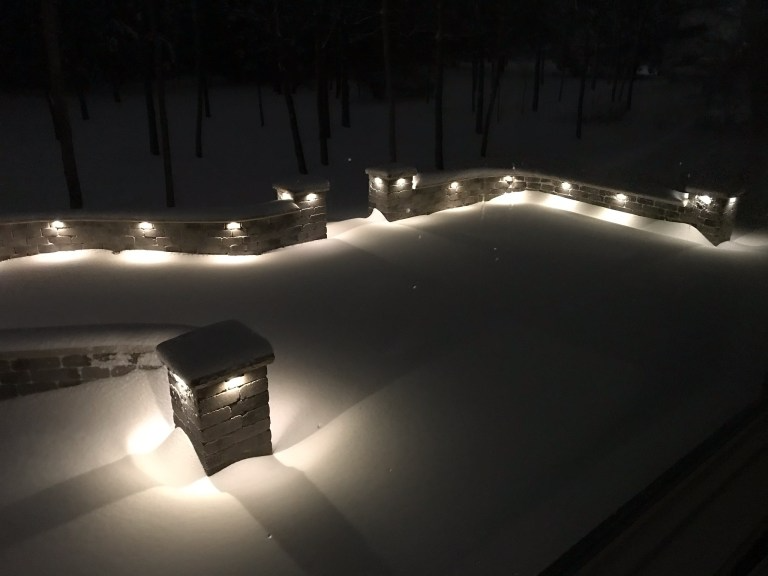 A snowy area with a stone wall and lights on it