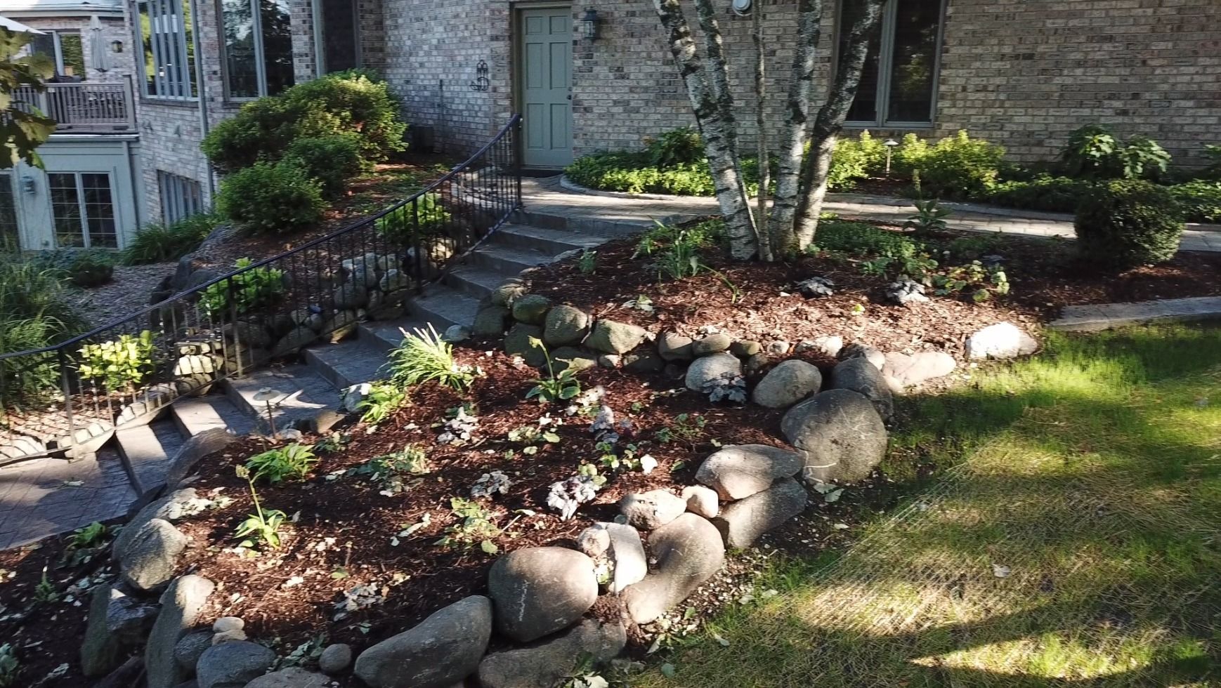 A brick house with a lush green lawn and rocks in front of it.
