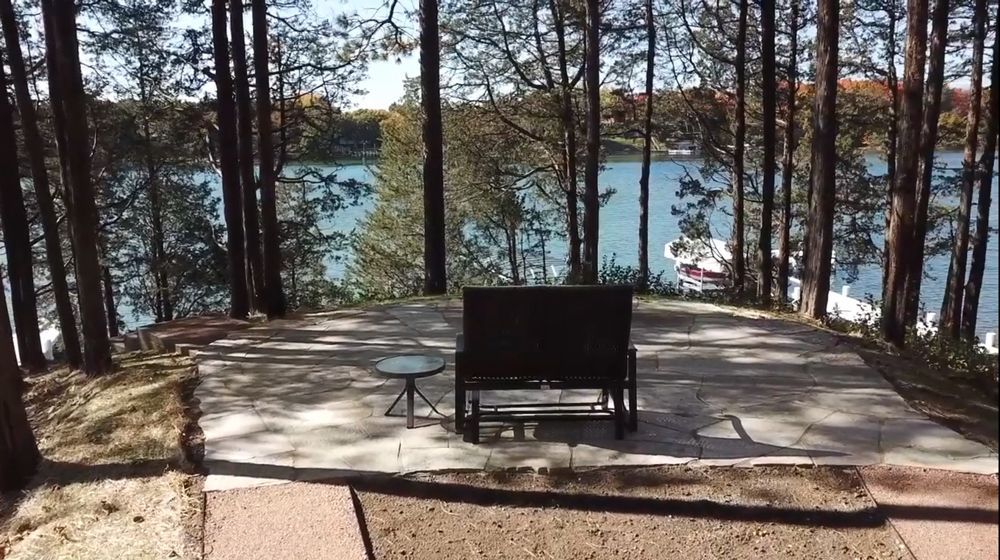 A bench sits on a patio overlooking a lake surrounded by trees.