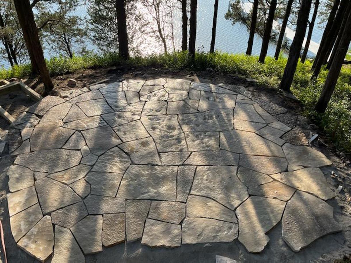 A stone patio with trees in the background and a lake in the background.