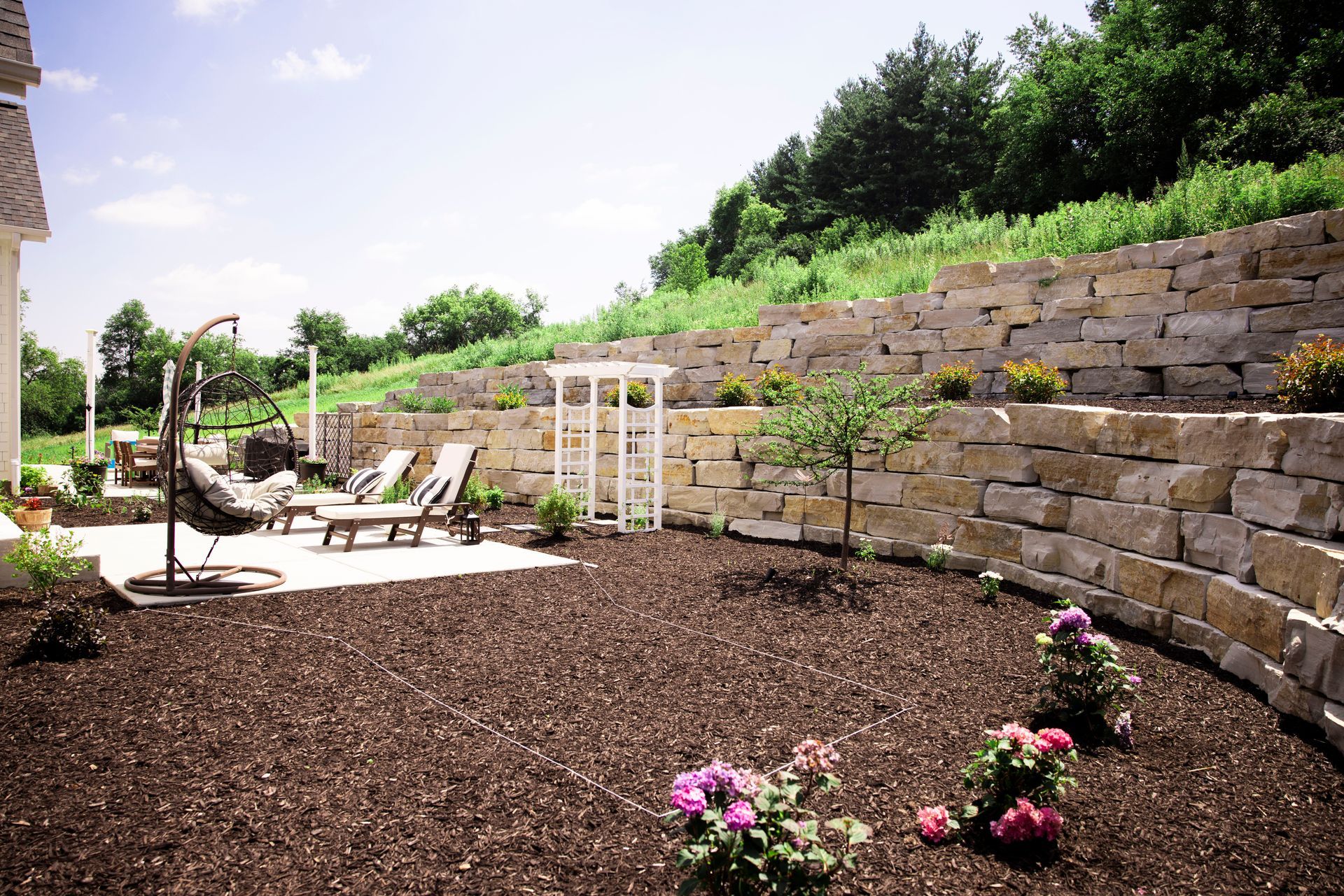 Stone retaining walls in a backyard with patio furniture and a small garden.