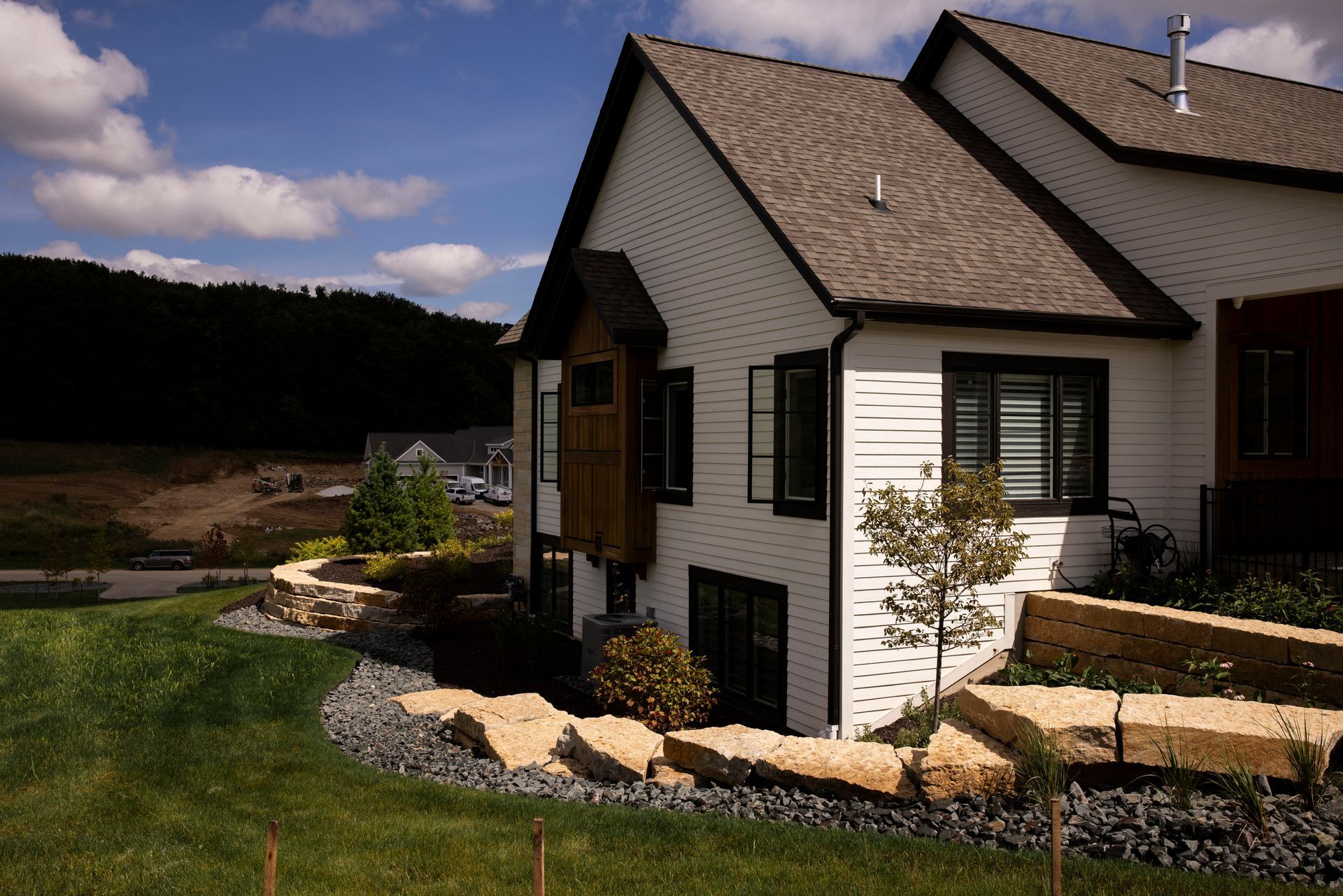 White house with dark trim and brown roof, set in a yard with landscaping and a blue sky.
