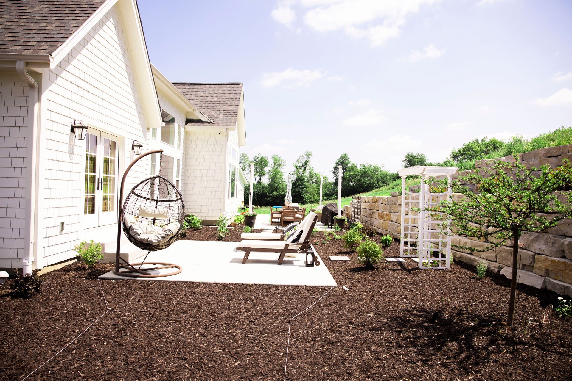 White house exterior with patio furniture, hanging chair, and landscaped yard.