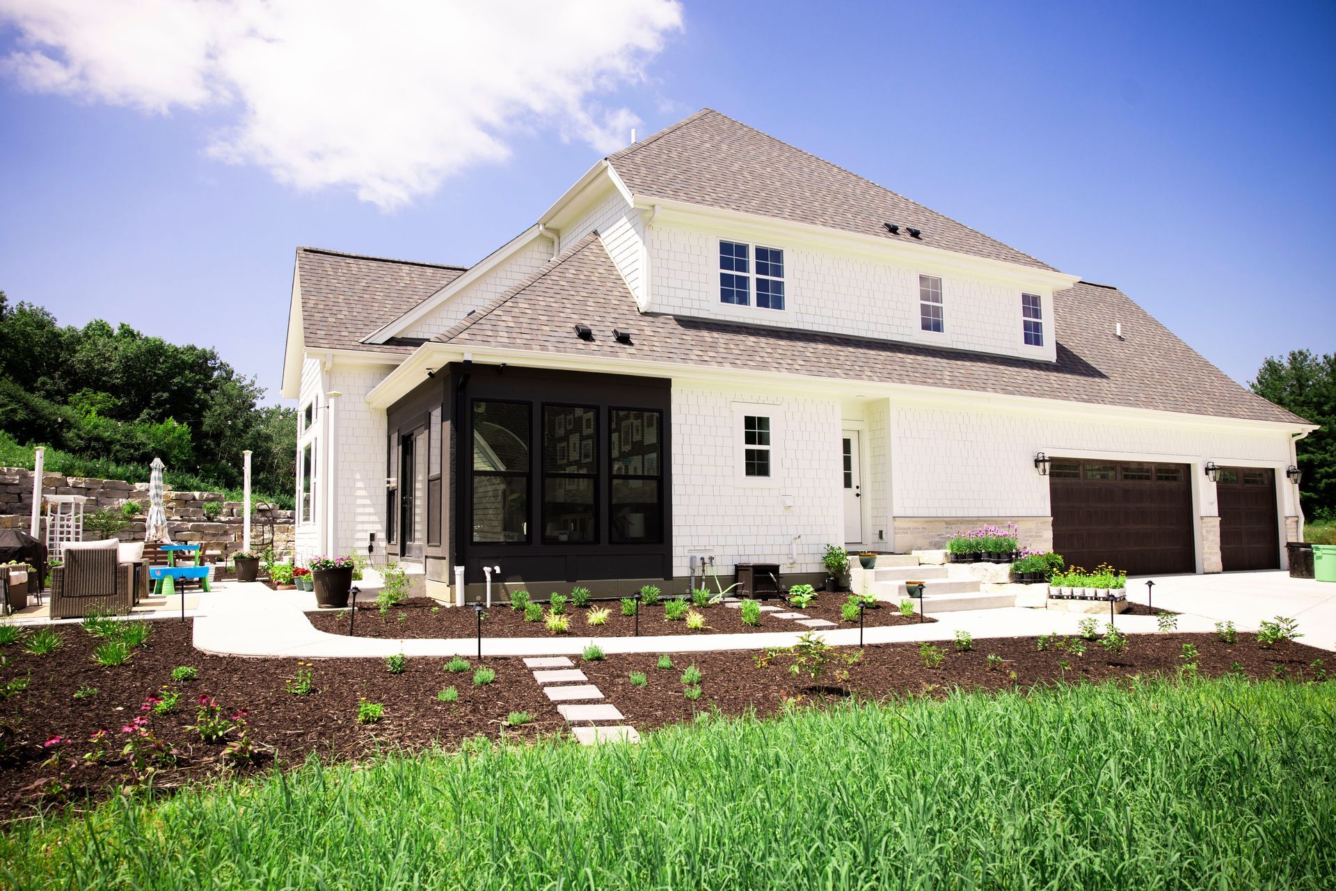 White house with dark trim and brown garage doors on a sunny day.