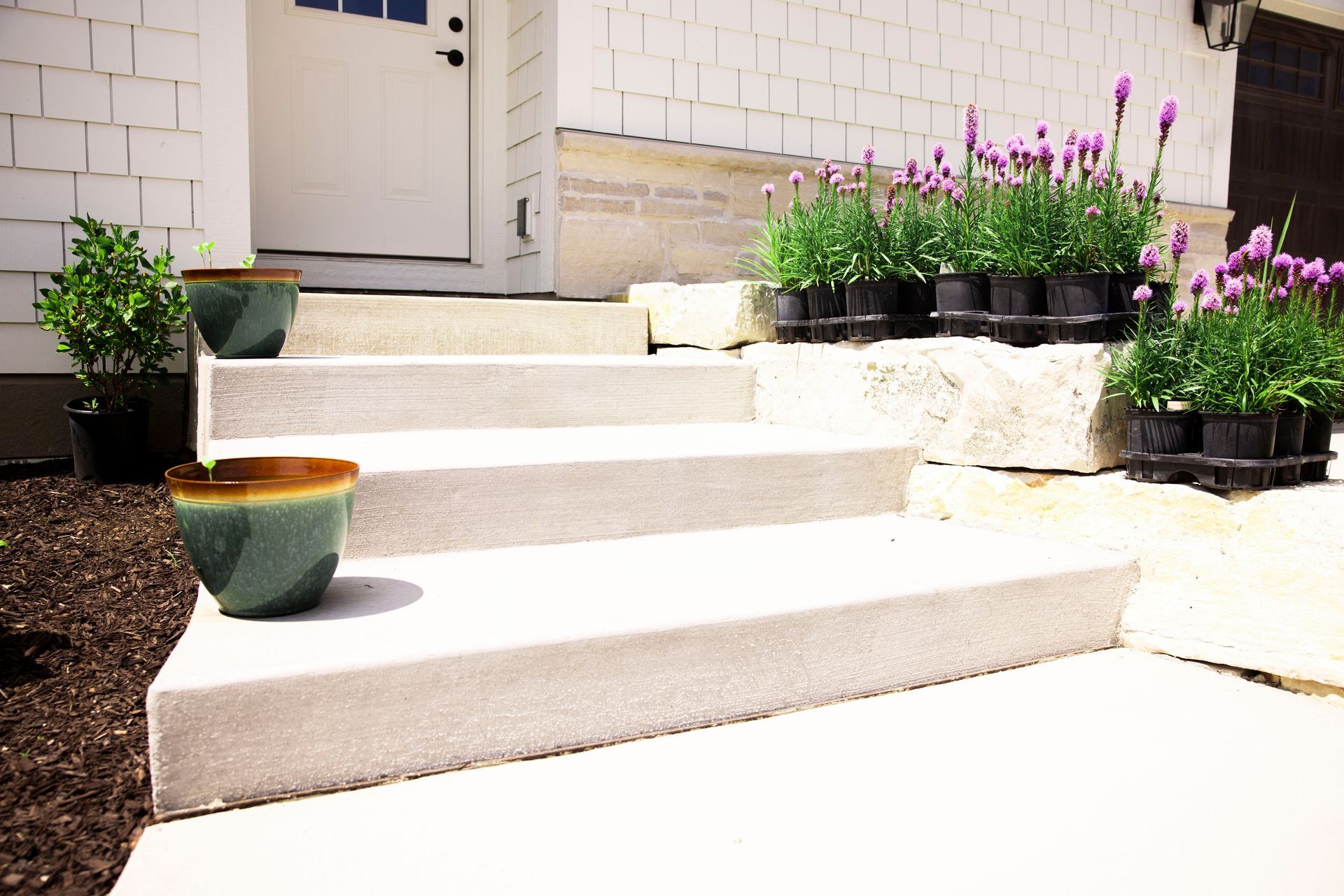 Concrete steps leading to a white door, flanked by potted plants and a stone garden bed with lavender.