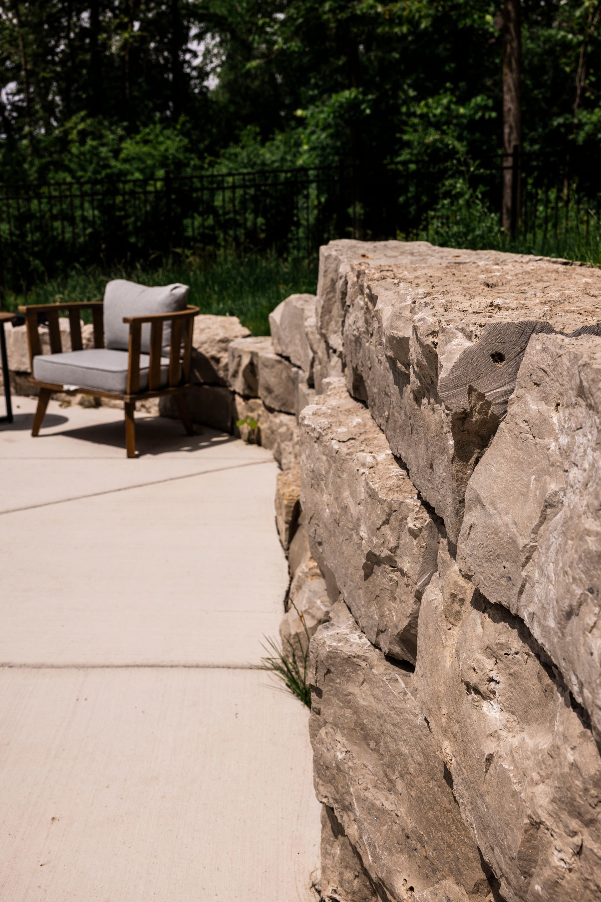 Stone retaining wall beside patio with wooden chair and cushions.