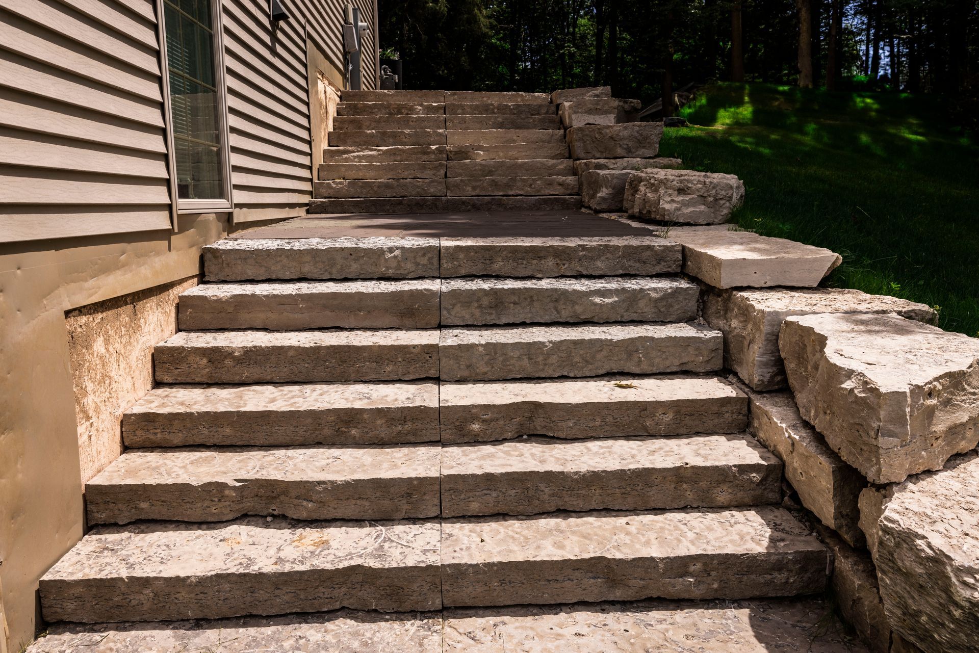 Stone steps leading up a slope next to a building, with large rock retaining walls on the sides.
