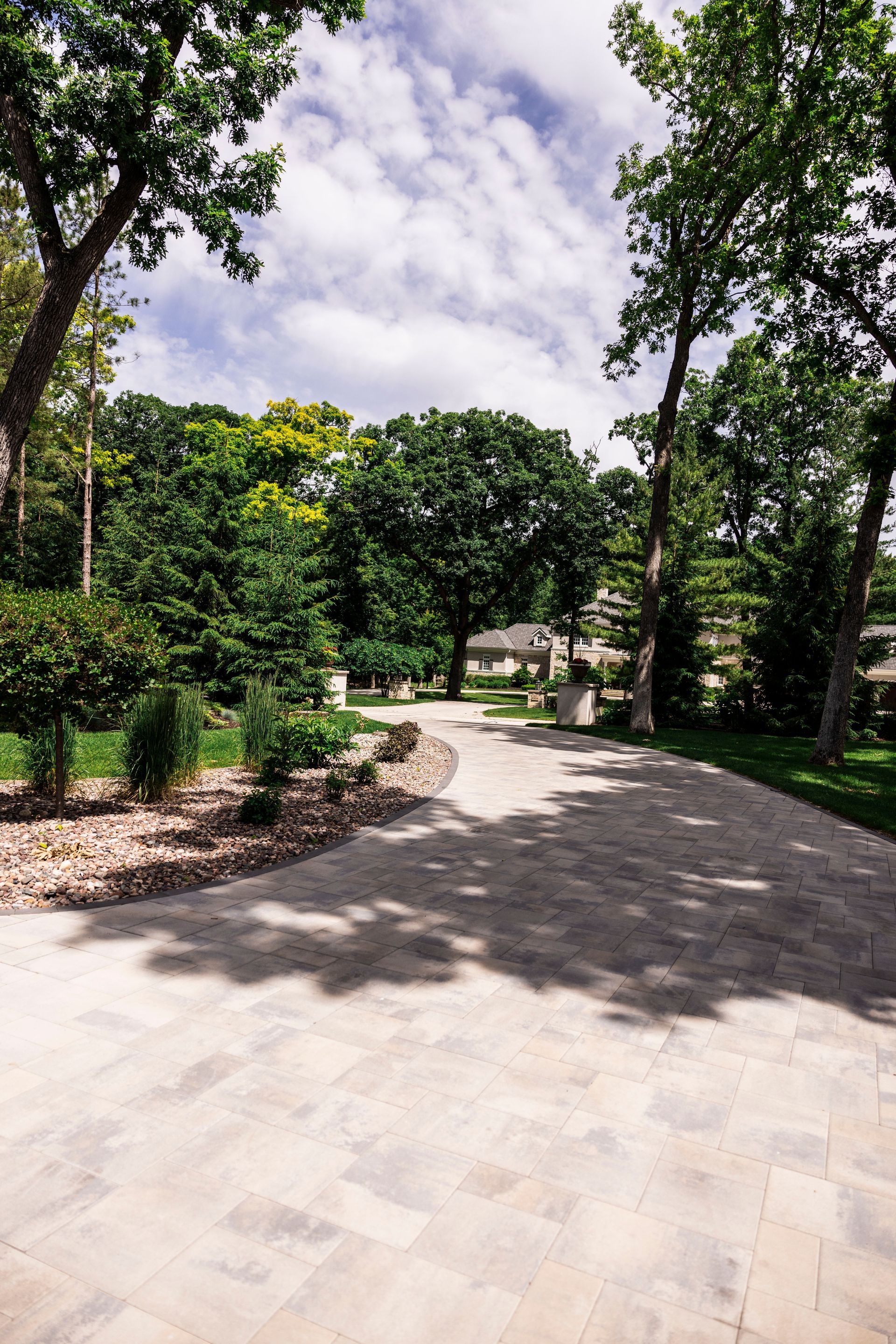 Brick pathway through a lush green park with trees and a cloudy sky.