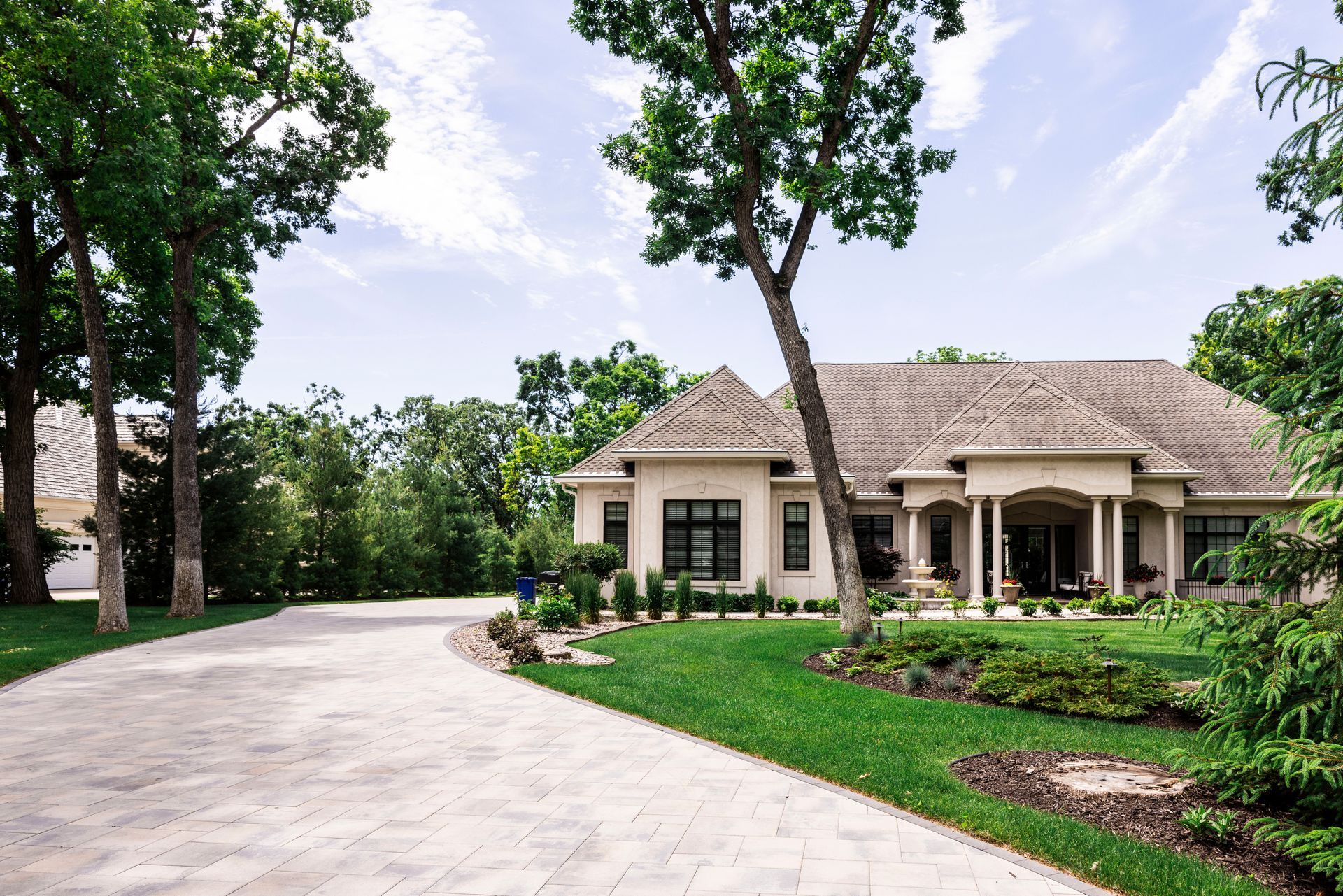 A light-colored house with a long driveway and lush green lawn, under a partly cloudy sky.