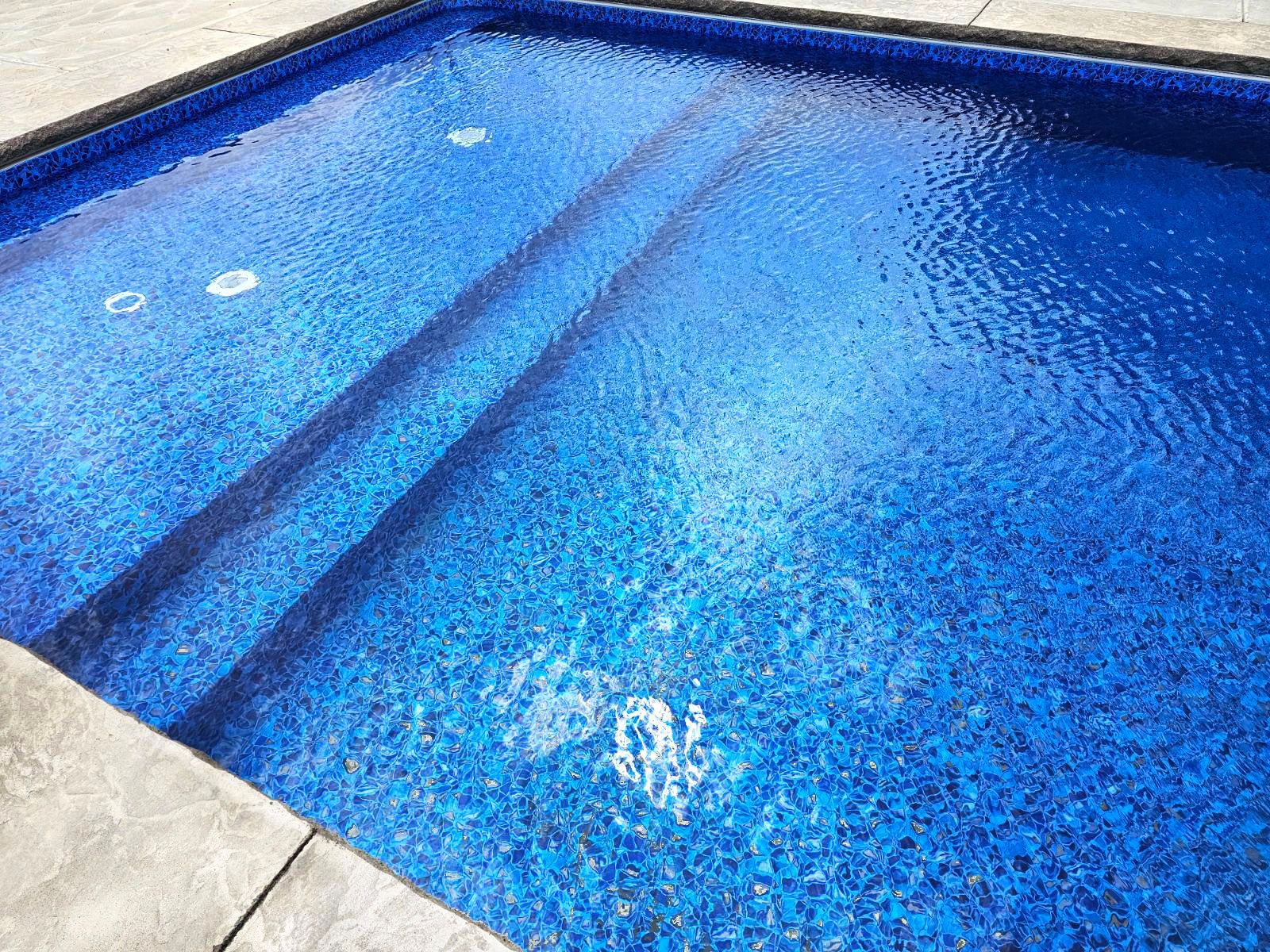Blue tiled swimming pool with steps, viewed from above.