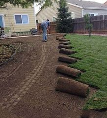 A man is laying rolls of turf in a backyard.