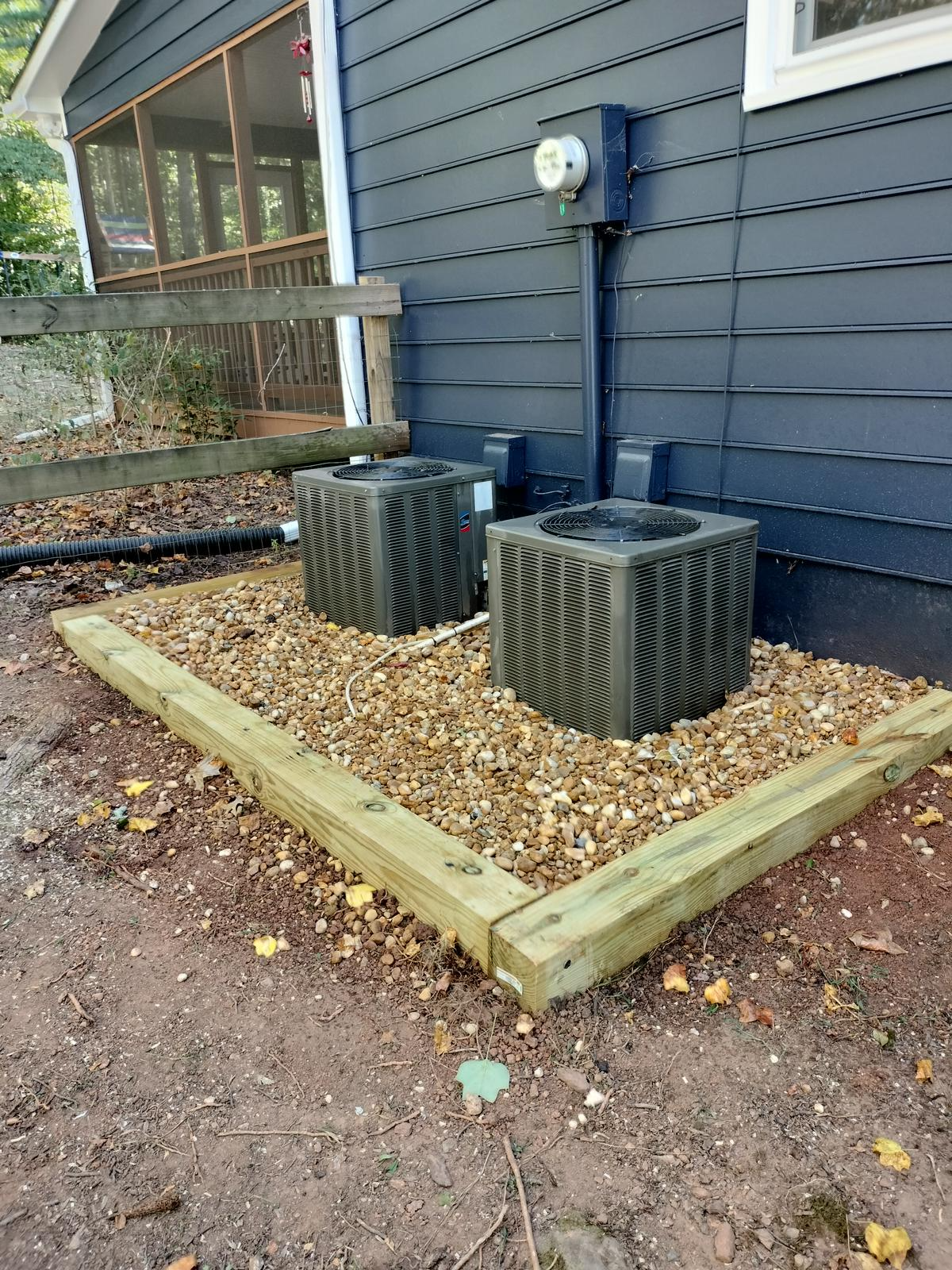 Two air conditioners are sitting on the side of a house.
