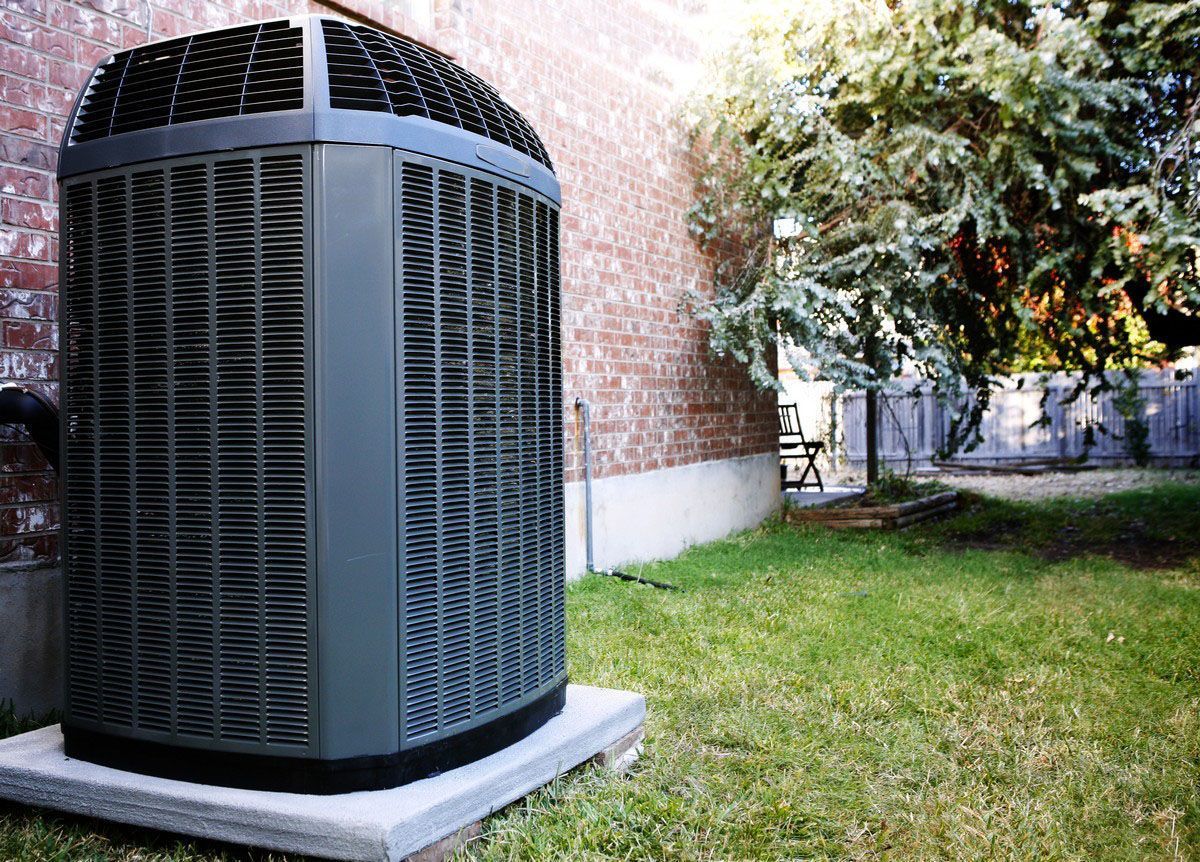 Air conditioning unit outside a brick building, on a concrete base, with green grass.