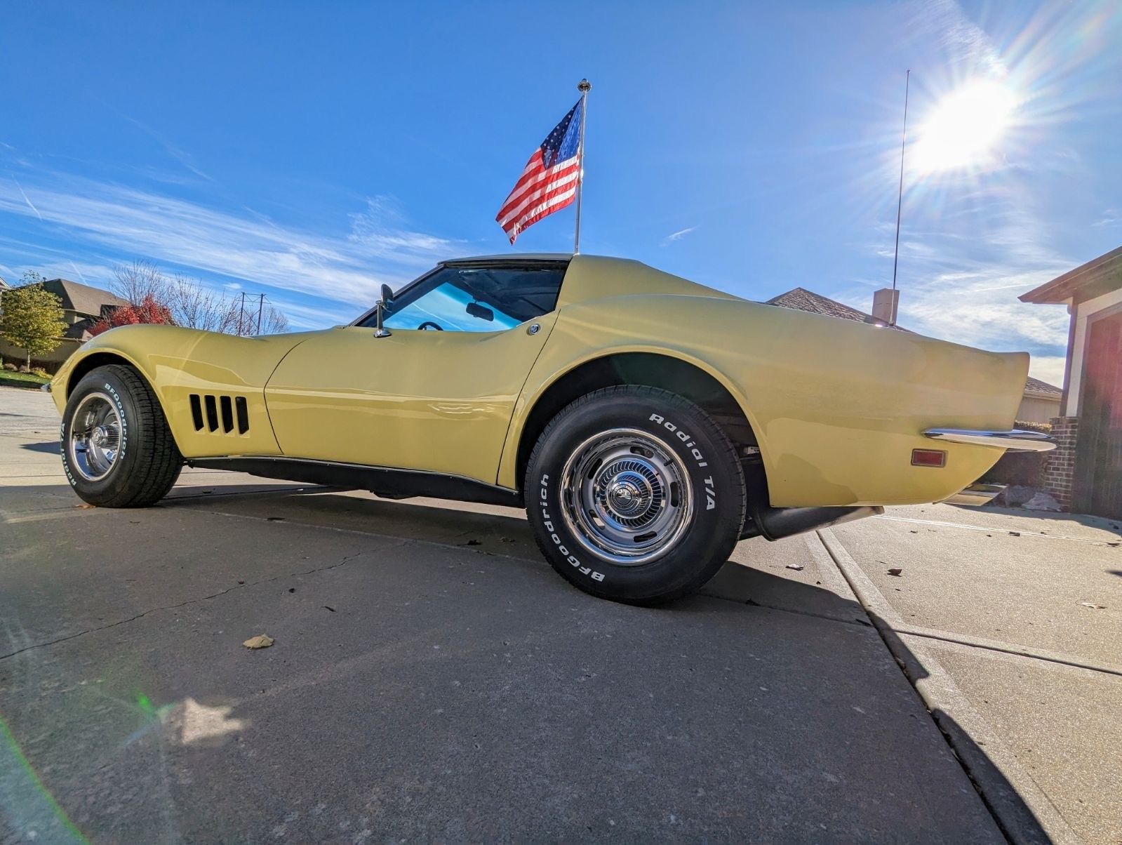 a yellow corvette is parked in a driveway with an American flag on top of it